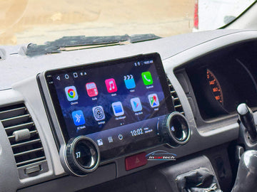 A 10.1-inch motor vehicle A/V player with dual knob control installed in a vehicle's dashboard, featuring a touchscreen interface displaying icons for Apple CarPlay and Android Auto.