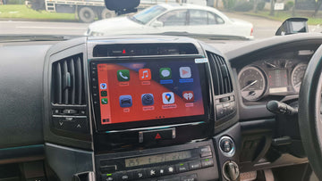 An aftermarket touch screen car stereo system displayed inside a vehicle's dashboard, featuring icons for Apple CarPlay and Android Auto.