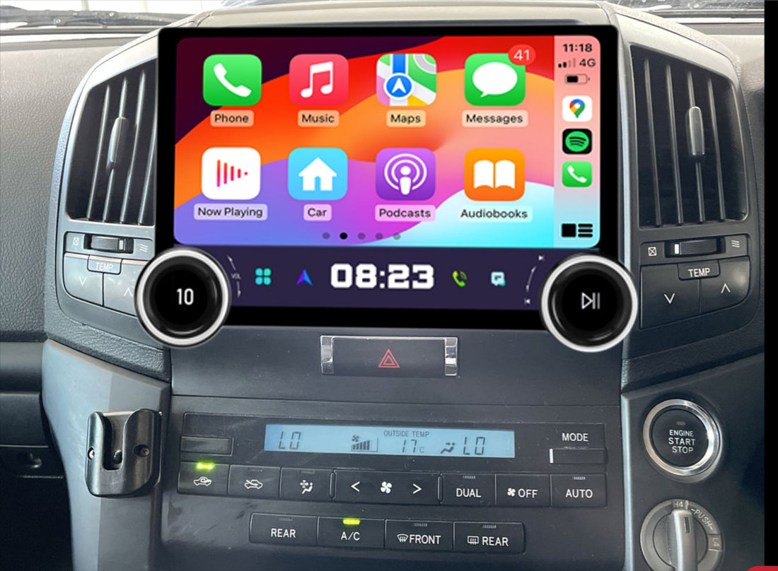 An aftermarket touch screen car stereo system interface displayed inside a vehicle's dashboard. The screen shows tiles for Apple CarPlay and Android Auto features such as phone, music, maps, messages, and others.